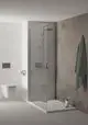 Duschsystem von Ideal Standard mit gläserner Trennwand, modernem Duschkopf und Wandarmatur. Handtuch hängt an der Wand. WC mit wandhängender Konstruktion in minimalistischem Badezimmer.